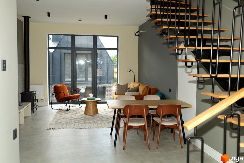 Сучасний інтер'єр вітальні з каміном, диваном та обідньою зоною. Великі вікна відкривають вид на зовнішній вигляд будинку.