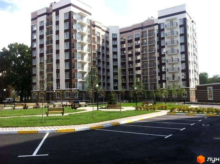 Житловий комплекс Центральний - багатоповерховий будинок з балконами та паркуванням. Навколо будинку розташований зелений двір з лавками та деревами.