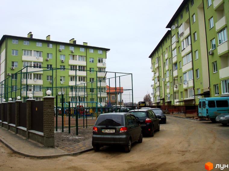 Житловий комплекс Смарагдове місто в Нових Петрівцях. Зелені багатоповерхові будинки з білими балконами та дитячим майданчиком.