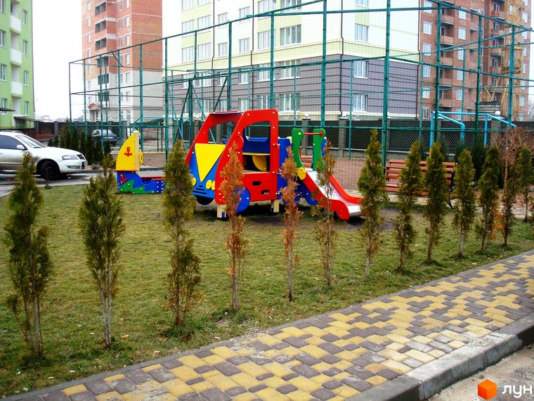 Новобудова ЖК Смарагдове місто в Нових Петрівцях. Дитячий майданчик з гіркою та гойдалкою на зеленій галявині біля будівель.