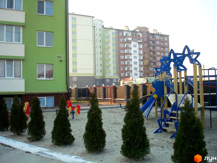 Житловий комплекс Смарагдове місто в Нових Петрівцях. Зелена багатоповерхівка з білими балконами та дитячий майданчик з гірками та гойдалками.
