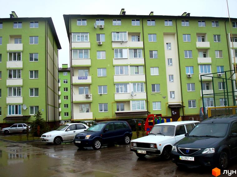 Житловий комплекс Смарагдове місто в Нових Петрівцях. Зелені багатоповерхові будинки з білими елементами, прибудинкова територія з автомобілями та дитячим майданчиком.