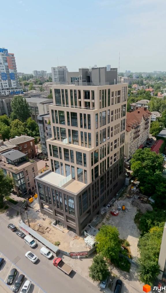 Житловий комплекс DeLight Hall з бежевими та темними фасадами. Поруч будівельний майданчик та вулиця з автомобілями.