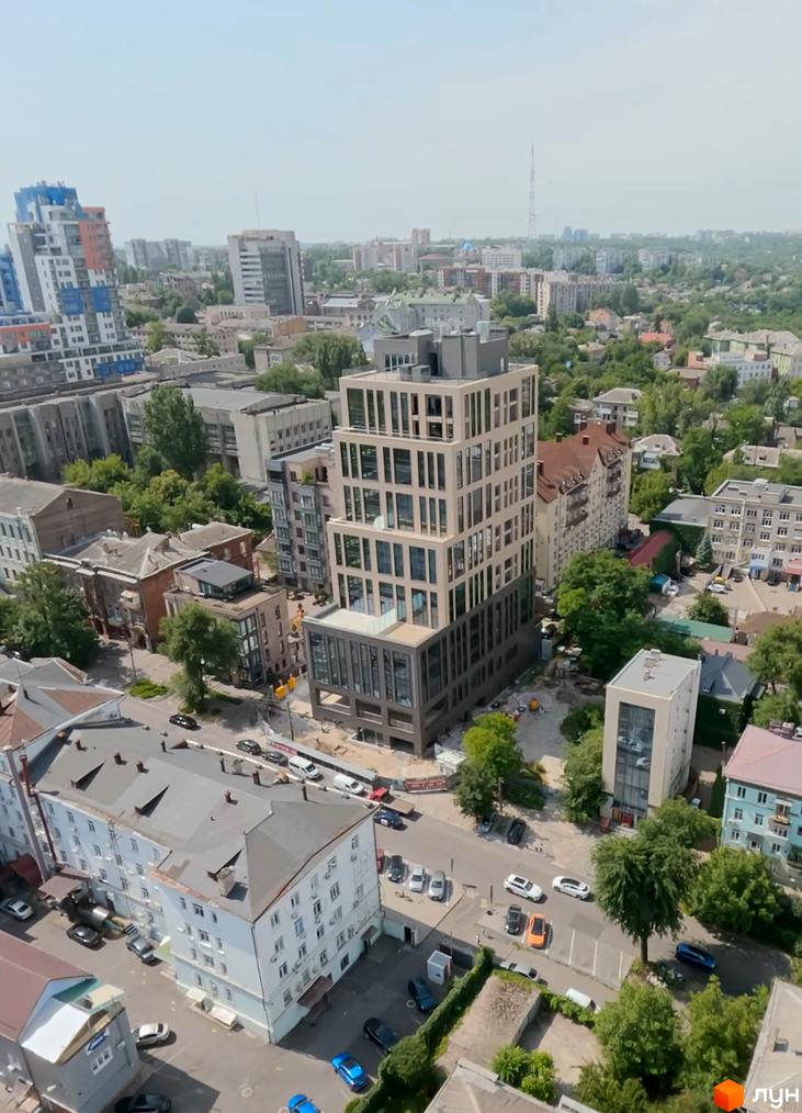 Житловий комплекс DeLight Hall має багатоповерхову світлу будівлю з темним цоколем та численними вікнами. Навколо розташовані міські забудови, дороги та зелені насадження.