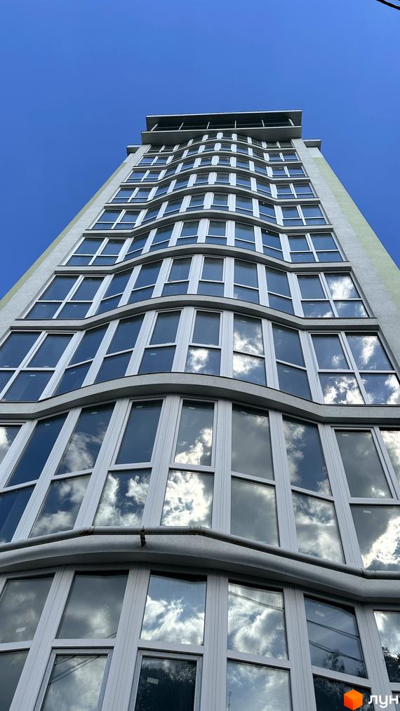 Житловий комплекс Потьомкінський. Висотна будівля з хвилястим фасадом та великою кількістю вікон, що відображають небо та хмари.