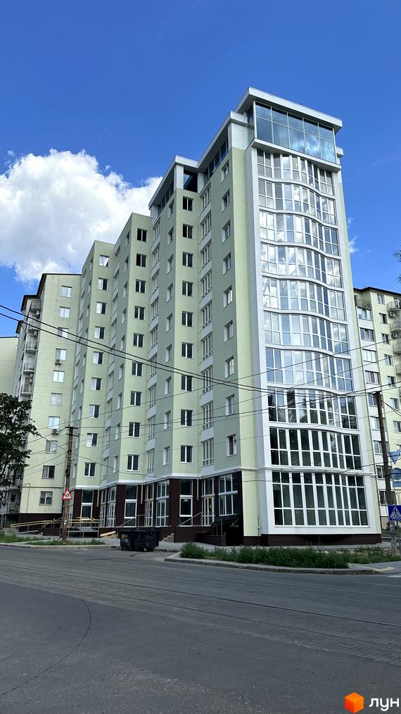 Зовнішній вигляд світло-зеленої новобудови ЖК Потьомкінський з великою кількістю вікон та скляним верхнім поверхом. Поруч проїжджа частина та зелені насадження.