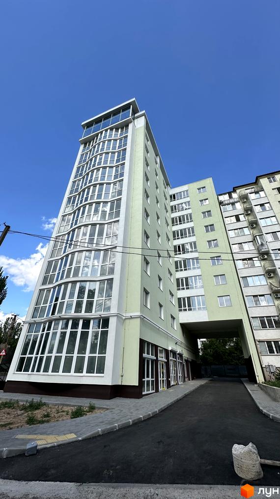 Зовнішній вигляд новобудови ЖК Потьомкінський з панорамними вікнами та світлою фасадною частиною. Прибудинкова територія облаштована тротуарною плиткою та асфальтованим проїздом.