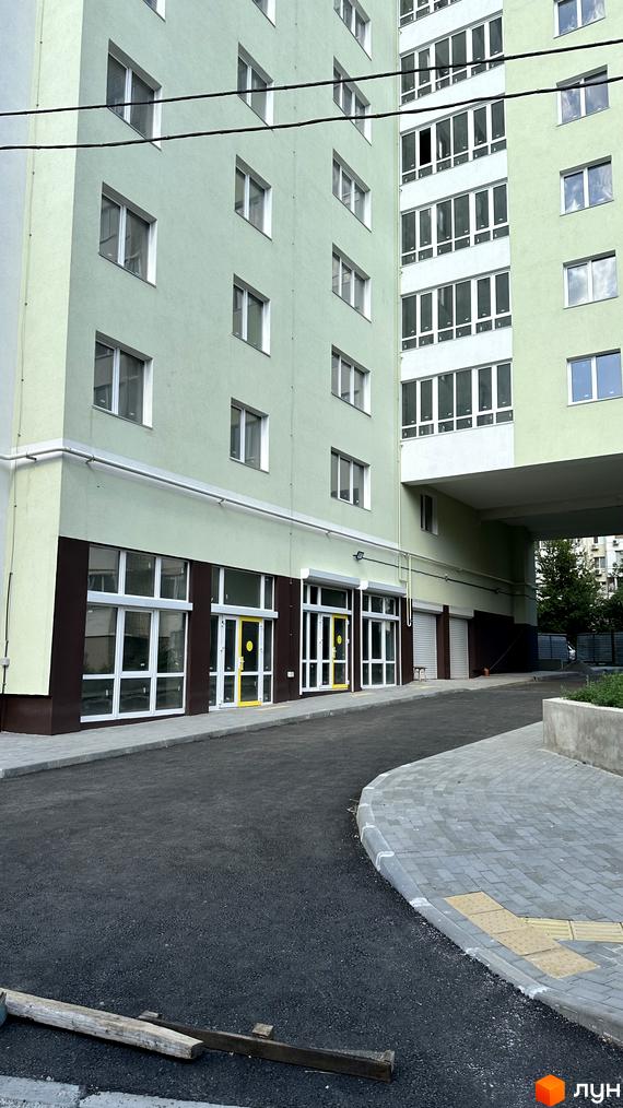 Зовнішній вигляд житлового комплексу Потьомкінський з зеленим фасадом та великими вікнами. Прибудинкова територія з асфальтованою дорогою та тротуаром.