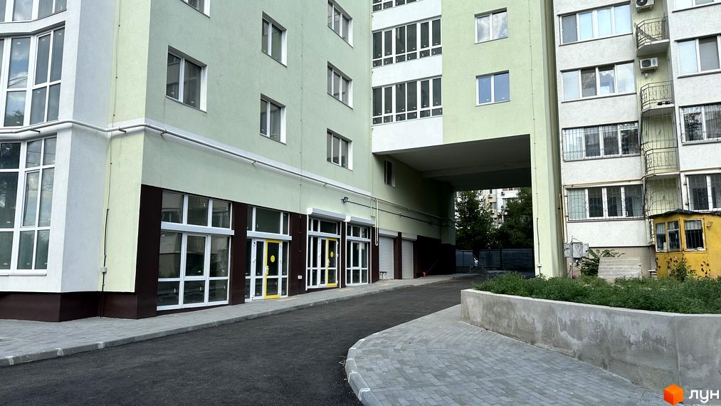 Житловий комплекс Потьомкінський. Зовнішній вигляд будинку з зеленими та світлими фасадами, великими вікнами та проїздом під аркою. Прибудинкова територія з бруківкою та зеленими насадженнями.