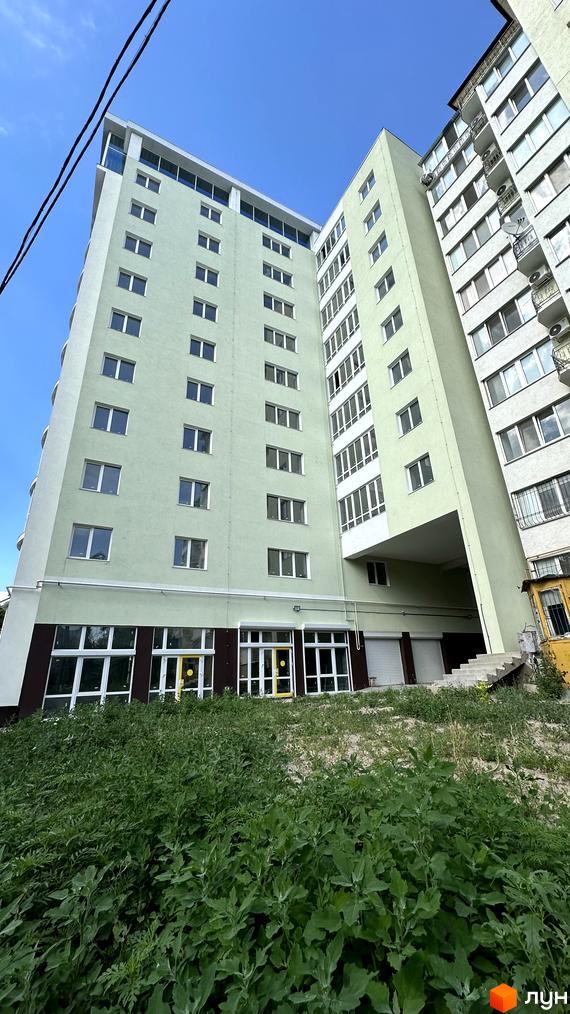 Зелена багатоповерхова новобудова ЖК Потьомкінський з білими вікнами та балконами. Навколо будинку зелені насадження та облаштована прибудинкова територія.