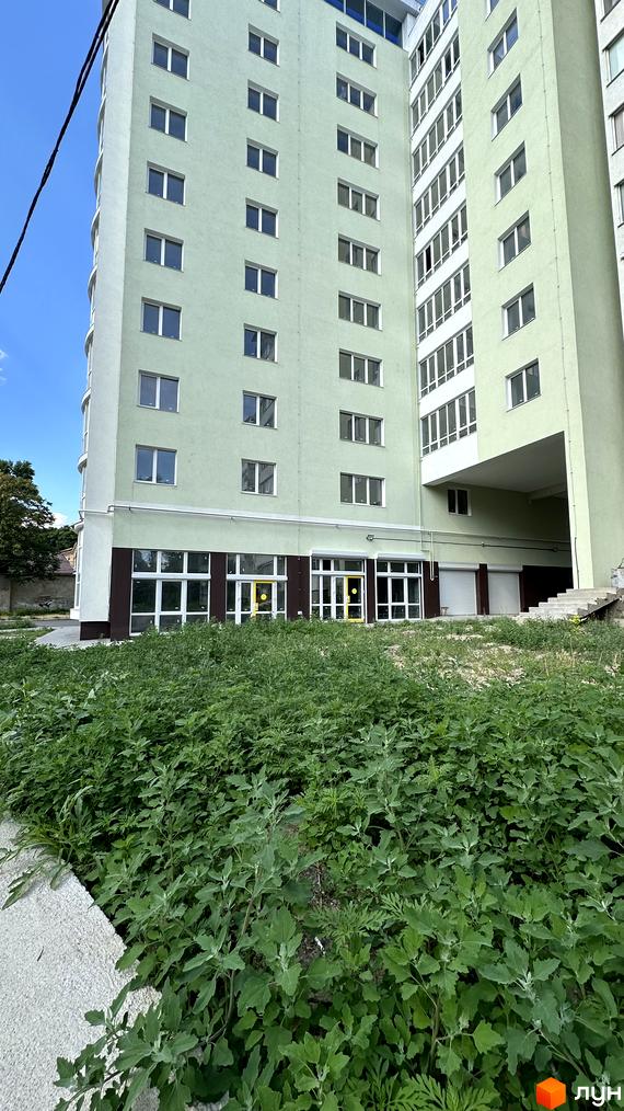 Зовнішній вигляд багатоповерхового будинку ЖК Потьомкінський світло-зеленого кольору з великою кількістю вікон. На передньому плані видно зелену зону з травою.