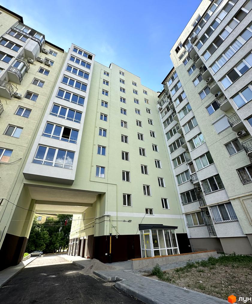 Зовнішній вигляд житлового комплексу Потьомкінський з світло-зеленими фасадами та великою кількістю вікон. На прибудинковій території видно арку для проїзду, зелені насадження та елементи благоустрою.