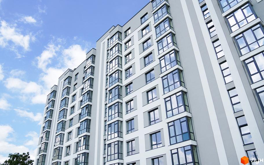 Новобудова Молодіжний з великою кількістю вікон та балконів, розташована на фоні блакитного неба з хмарами.