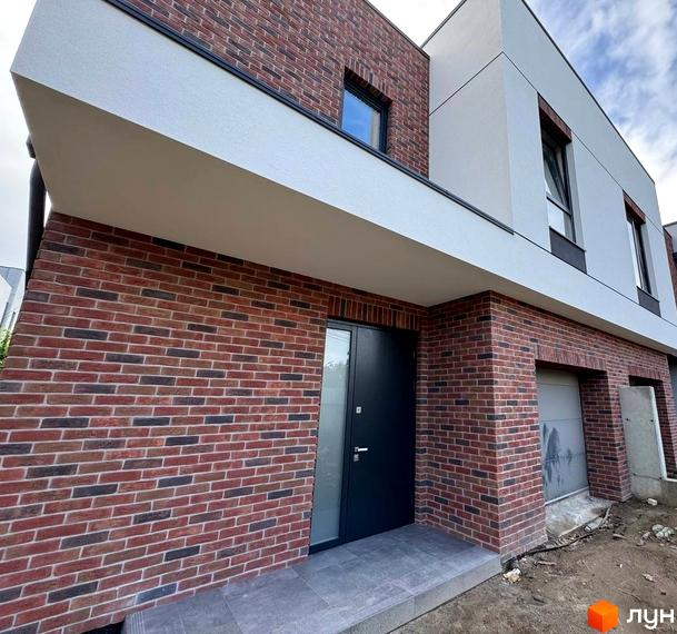 Таунхауси Loft House з фасадом з цегли та білої штукатурки. Зовнішній вигляд будинку з дверима та гаражем.