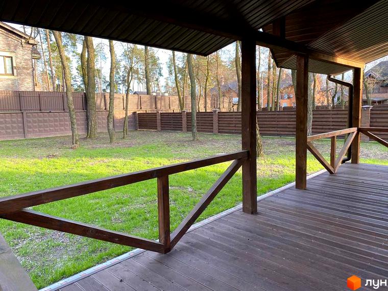 Котеджне містечко КМ Парк хаус: вид з тераси на зелену галявину та паркан. Навколо ростуть дерева, видно будинки.
