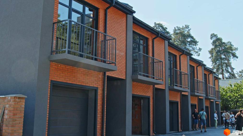 Зовнішній вигляд таунхаусів Позітано Центр з цегляним фасадом та балконами. Поруч розташовані дерева та кілька людей.