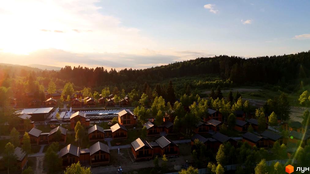 Котеджне містечко KM PHOENIX MEDICAL RESORT з дерев'яними будиночками та басейном на фоні лісу. Територія комплексу оточена зеленню та деревами.