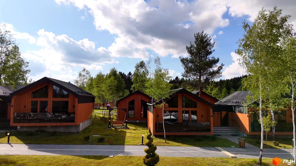 Котеджне містечко PHOENIX MEDICAL RESORT з дерев'яними фасадами та великими вікнами, оточене зеленню та деревами. На території розташовані доріжки, газони та елементи ландшафтного дизайну.