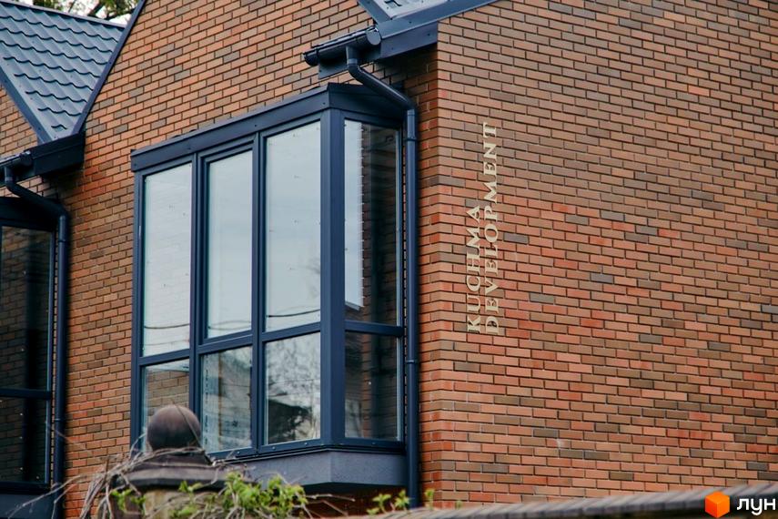 Фасад цегляного будинку з великими вікнами в Котеджному містечку Positano Park. На стіні назва забудовника KUCHMA DEVELOPMENT.