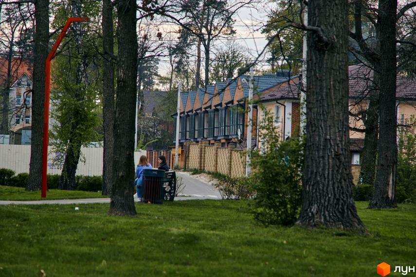 Вигляд Котеджного містечка Positano Park з деревами на передньому плані та будинками на задньому. Зелена трава на території.