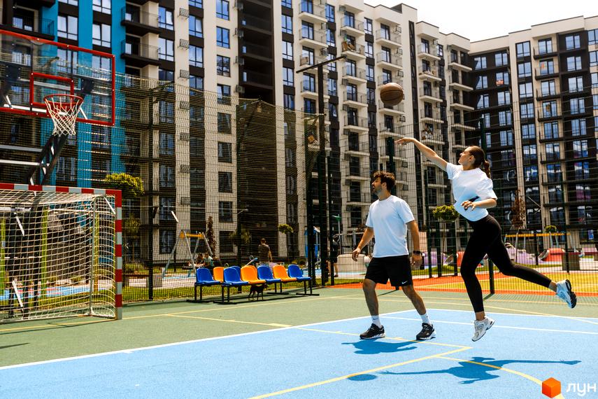 Зображення Житлового комплексу Family Plaza з баскетбольним майданчиком. На передньому плані пара грає з м'ячем.