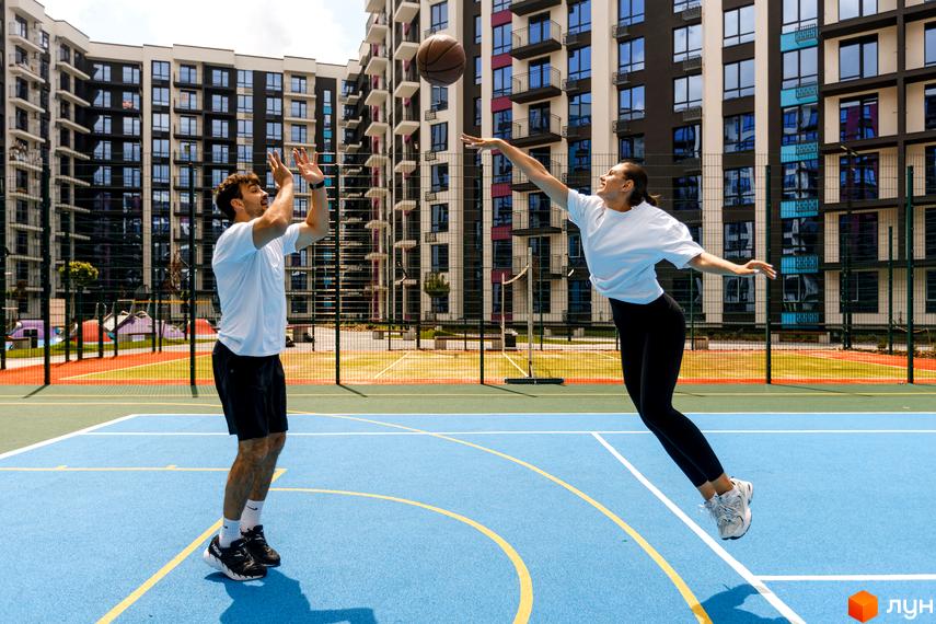 Зображення Житлового комплексу Family Plaza: люди грають в баскетбол на спортивному майданчику біля багатоповерхового будинку.