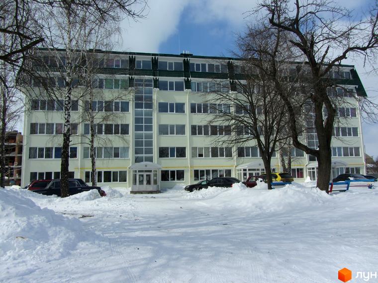 Зовнішній вигляд світлої багатоповерхової новобудови ЖК Милі квартири взимку. Навколо будинку засніжена територія з деревами та припаркованими автомобілями.