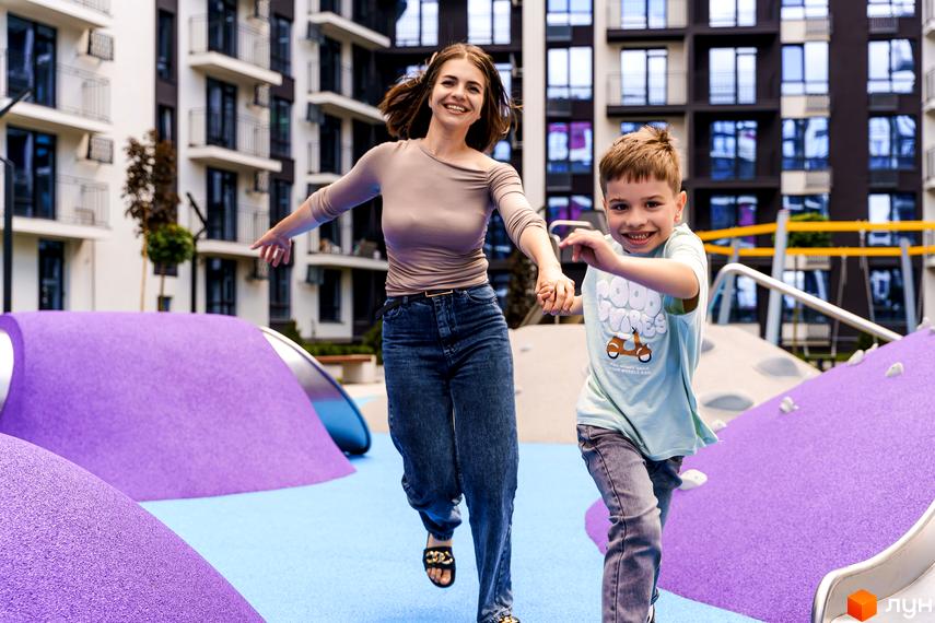 Житловий комплекс Family Plaza з дитячим майданчиком. На фото мати з сином тримаються за руки та біжать на ігровому майданчику.