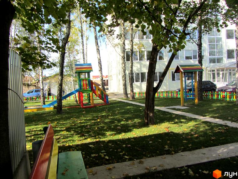 Житловий комплекс Милі квартири. Дитячий майданчик та зелена зона біля багатоповерхового будинку з великими вікнами.