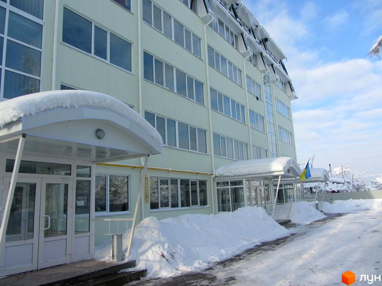 Зовнішній вигляд житлового комплексу Милі квартири взимку, з великою кількістю снігу на прибудинковій території та навісами над входами. Будівля має багато вікон та кілька поверхів.