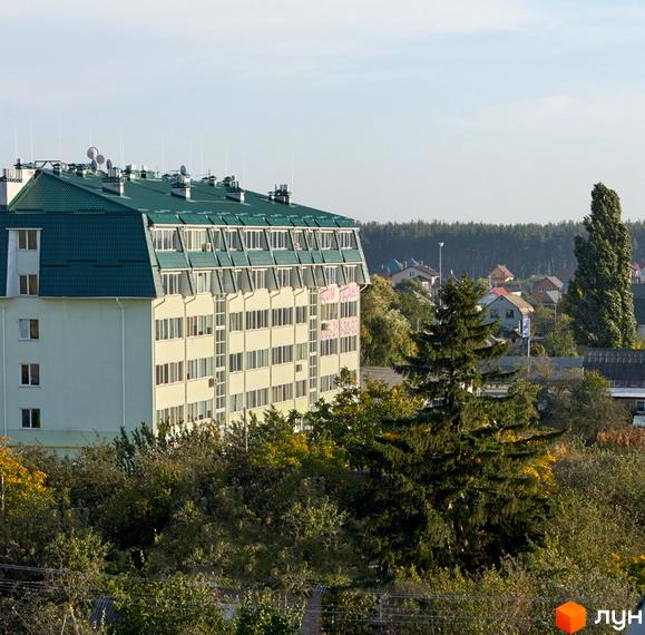Зовнішній вигляд багатоповерхового будинку з зеленим дахом. Навколо будинку розташовані дерева та інші будівлі.