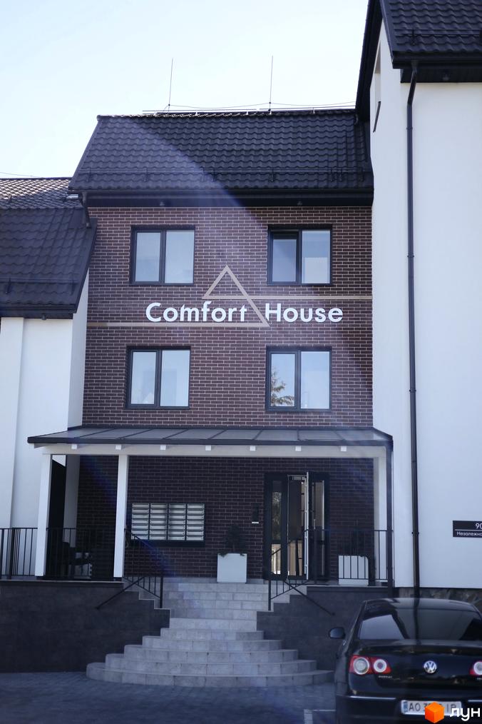 Фасад житлового комплексу Comfort House з цегляним оздобленням та сходами. Біля будинку розташований автомобіль та прибудинкова територія.