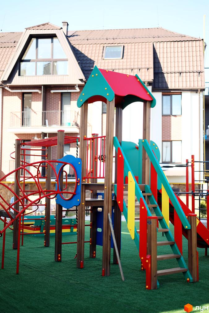 Житловий комплекс Comfort House з дитячим майданчиком на зеленій території. Сучасна архітектура будинків з коричневим дахом та великими вікнами.