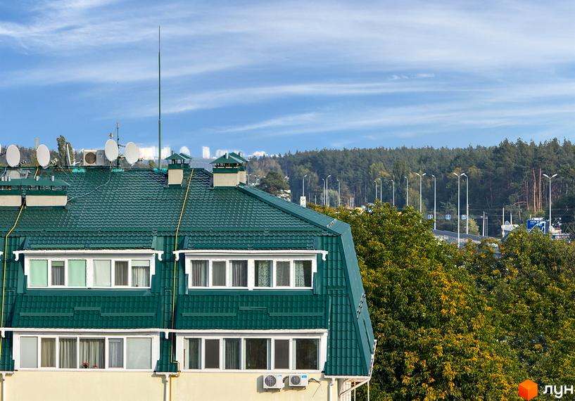 Зовнішній вигляд новобудови ЖК Милі квартири з зеленим дахом та вікнами. Навколо будинку розташовані дерева та міський пейзаж.