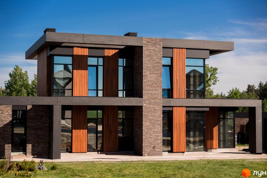 Котеджне містечко 9 ЕЛЕМЕНТІВ. Будинок з пласким дахом, фасадом з комбінації цегли, дерев'яних панелей та великих вікон. Навколо зелений газон.