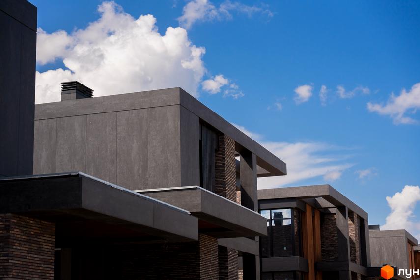 Будинки Котеджного містечка 9 ЕЛЕМЕНТІВ з сірими фасадами, цегляними вставками та великими вікнами на тлі блакитного неба.