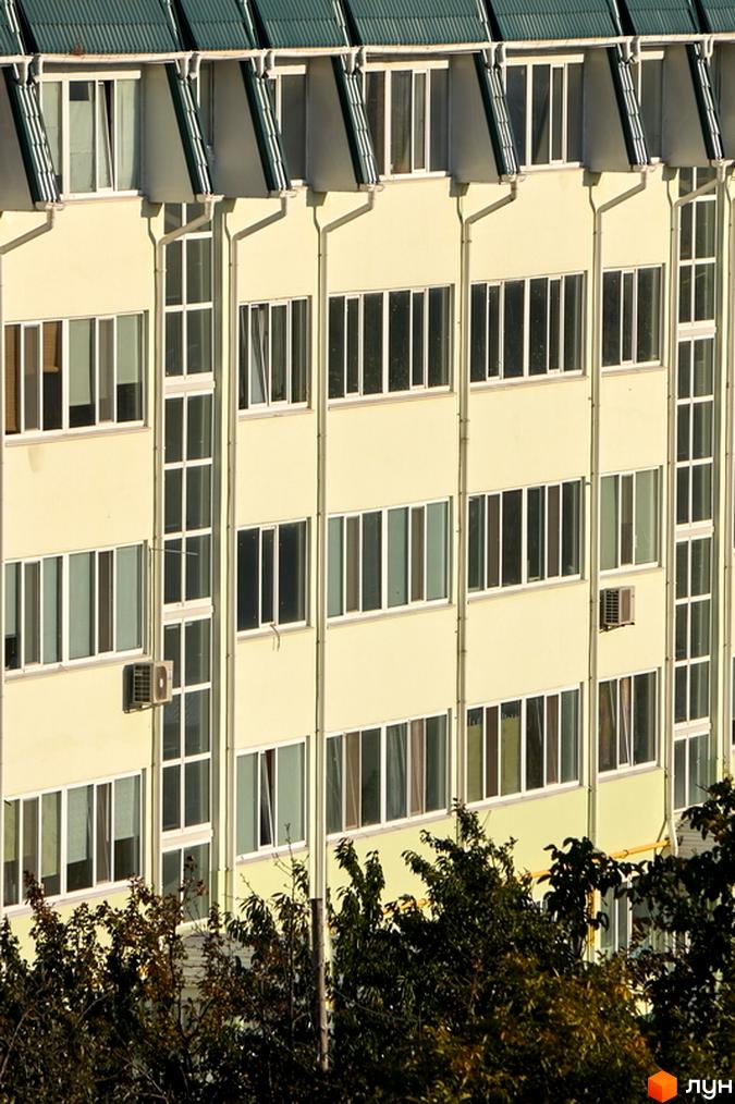 Фасад житлового комплексу Милі квартири з численними вікнами та кондиціонерами. Зелена покрівля та дерева на передньому плані.