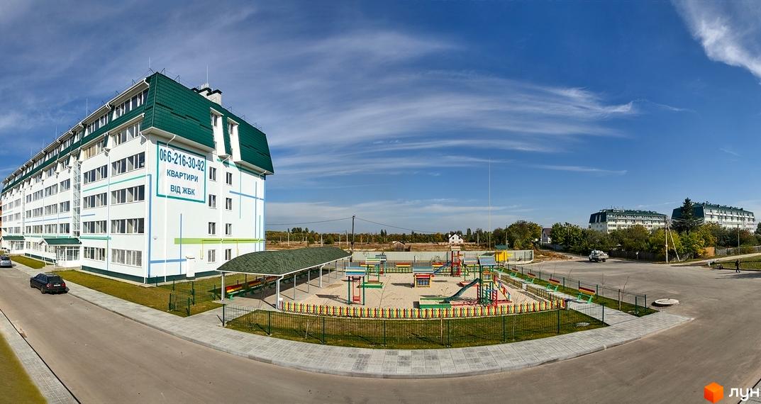 Житловий комплекс Милі квартири - біла багатоповерхівка із зеленим дахом та дитячим майданчиком. Зовнішній вигляд будинку та прибудинкова територія.