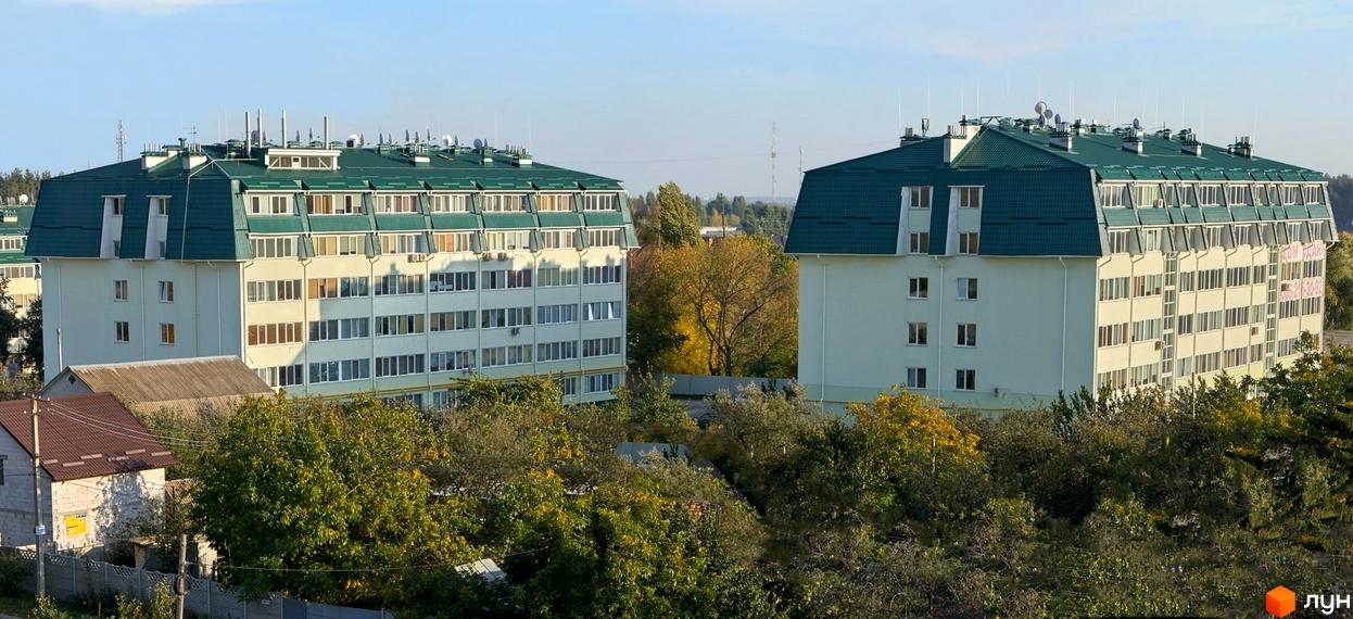 Фото новобудови ЖК Милі квартири. Зовнішній вигляд будинку з зеленим дахом та численними вікнами. Навколо будинку дерева та прибудинкова територія.