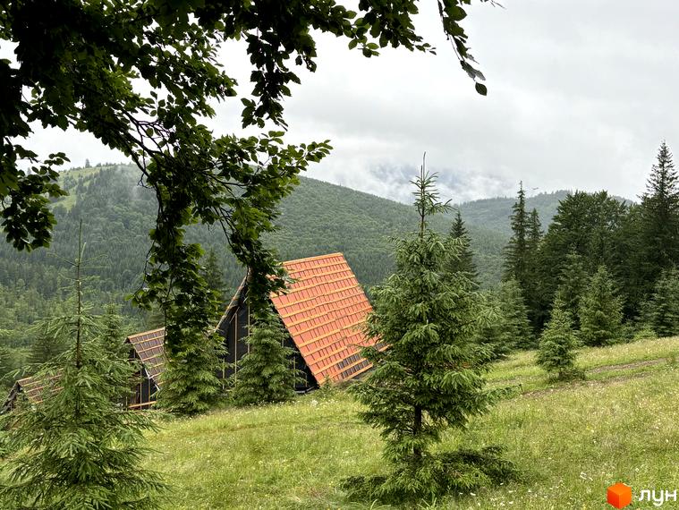 Комплекс відпочинку УЛІС - дерев'яні будинки з червоними дахами на тлі гірського пейзажу. Навколо зелені ялини та трава.