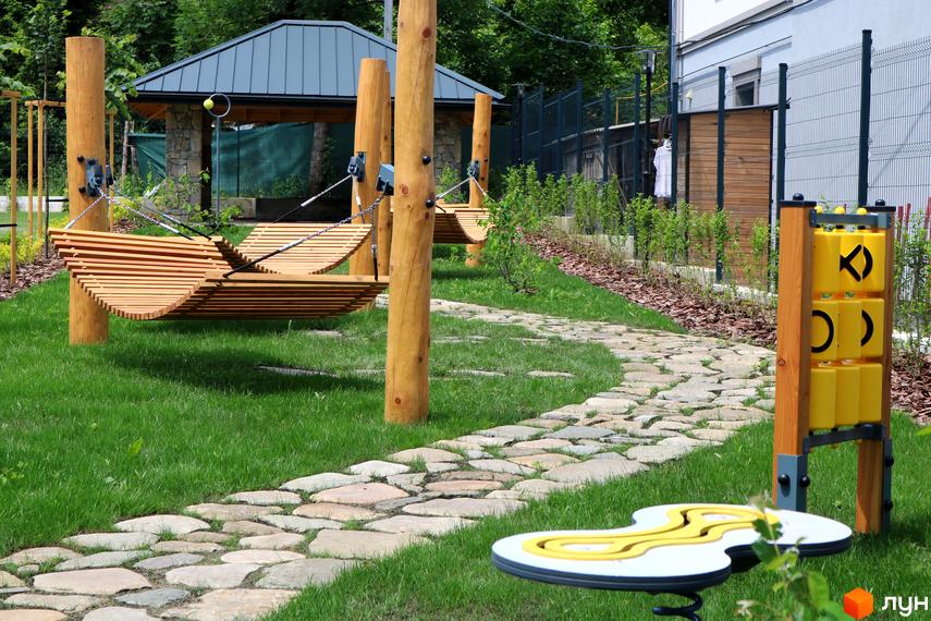 Житловий комплекс Крайобраз: дитячий майданчик з дерев'яними гойдалками та пішохідною доріжкою з каменю. Сучасне облаштування території житлового комплексу.