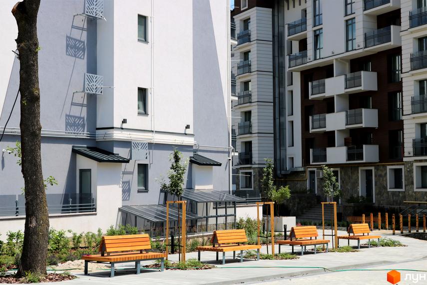 Житловий комплекс Крайобраз. Сучасні фасади будівель та облаштована прибудинкова територія з лавками та деревами.