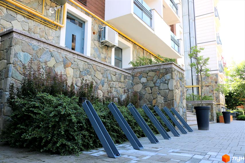 Житловий комплекс Крайобраз з кам'яною облицовкою фасаду та зеленою прибудинковою територією. На території встановлено велопарковку.