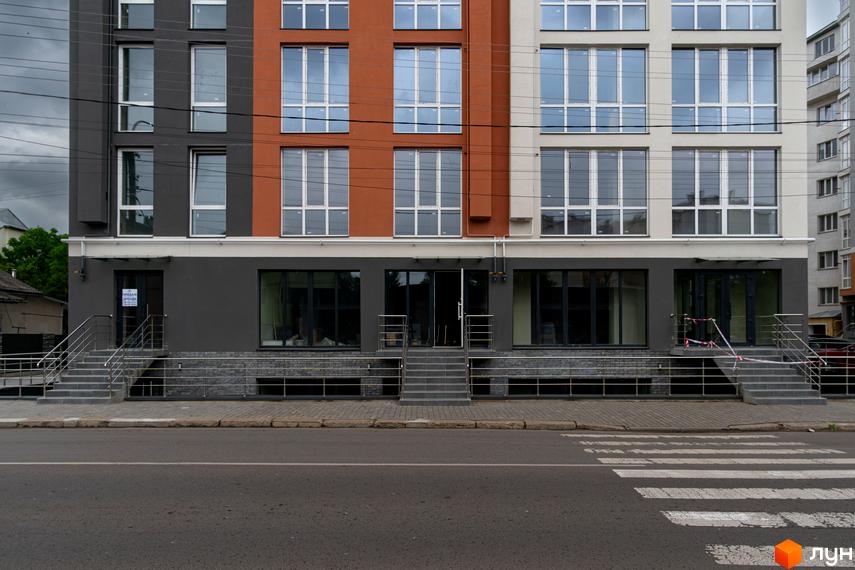 Новобудова ЖК Затишний з фасадом з сірого та теракотового кольорів. Перед будинком розташовані сходи та тротуар з пішохідним переходом.