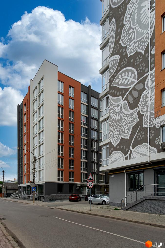 Зовнішній вигляд будинку ЖК Затишний з цегляними та білими фасадами. Поруч дорога та тротуар.