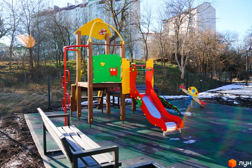 Багатоповерхові будинки Житлового комплексу Затишний на тлі, з облаштованим дитячим майданчиком та гірками на передньому плані.