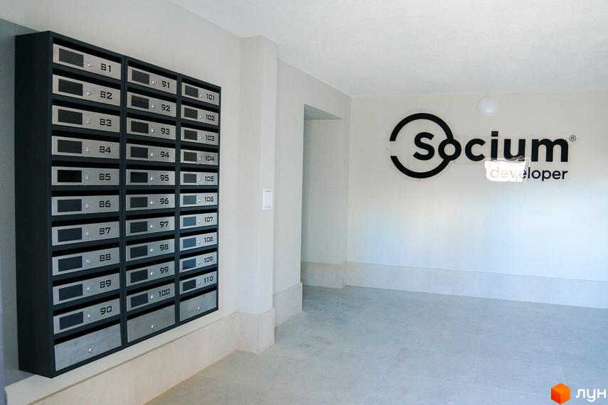 Комплекс з поштовими скриньками та логотипом Socium developer. Світлий коридор з сірою плиткою на підлозі.