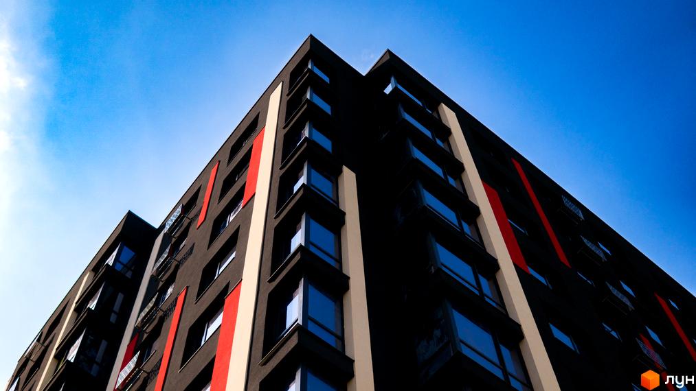 Житловий комплекс Union: темний фасад будівлі з червоними та світлими вертикальними елементами на тлі синього неба.