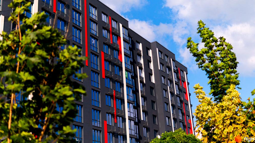 Новобудова ЖК Union з темним фасадом та червоними смугами на тлі блакитного неба з хмарами. Навколо будівлі зелені дерева.