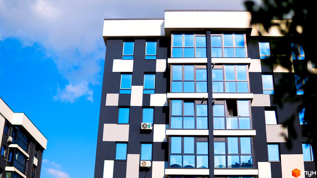 Зовнішній вигляд новобудови ЖК Union з панорамними вікнами та контрастним фасадом у сіро-білих тонах. Будинок розташований на фоні блакитного неба з хмарами.